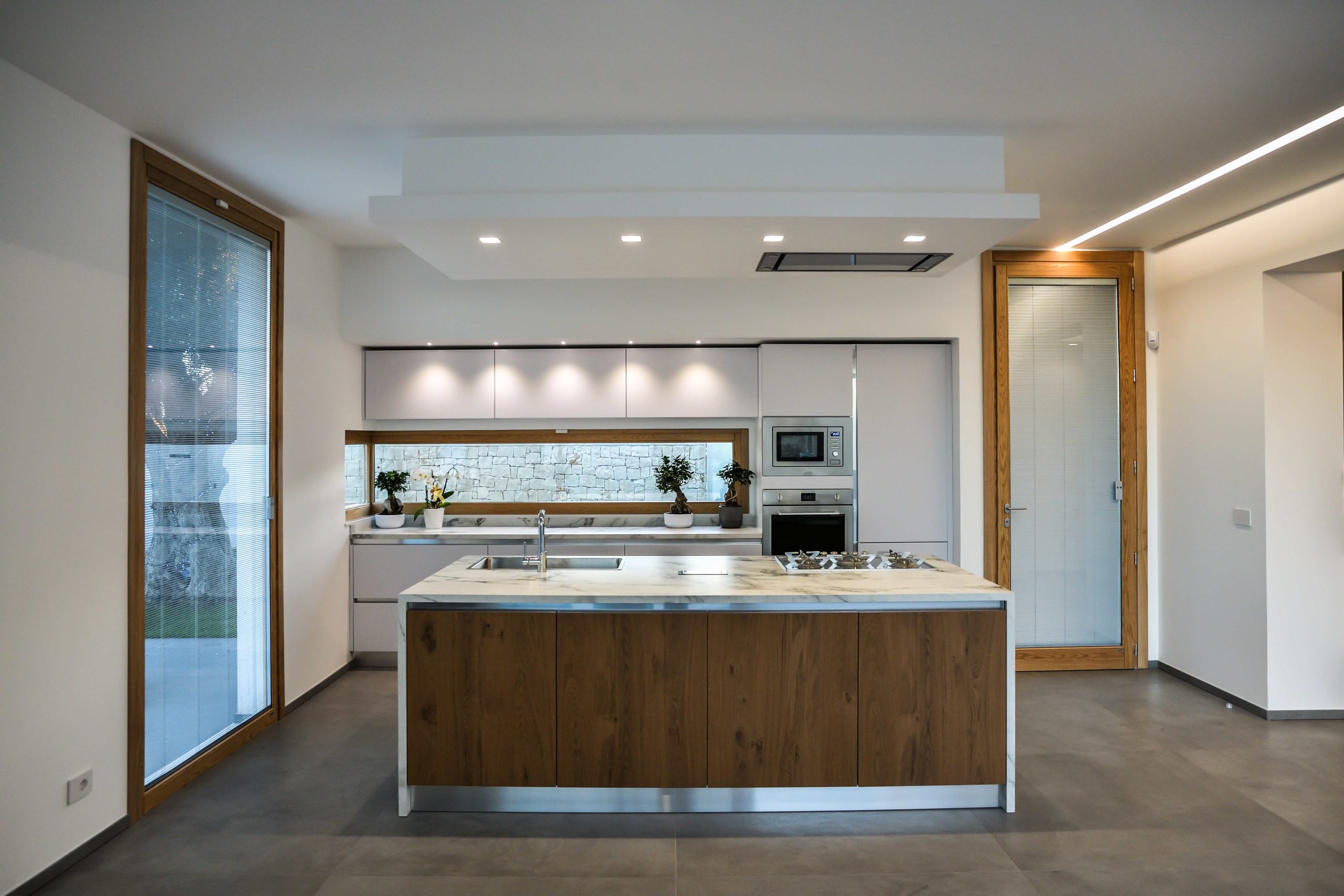 1. Cucina a parete laccata bianco opaco con top in gres, isola in rovere nodato con top e laterali in gres-min